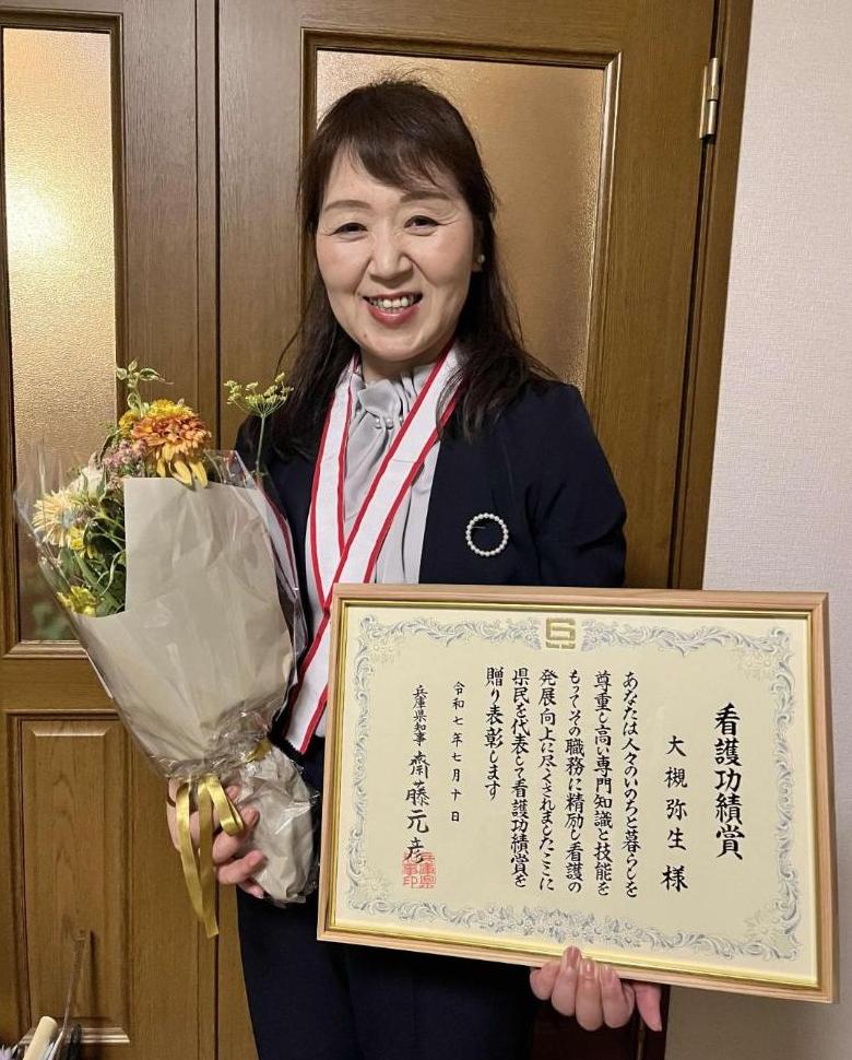 「看護功績賞」の賞状と花束を手ににこやかな先生の写真