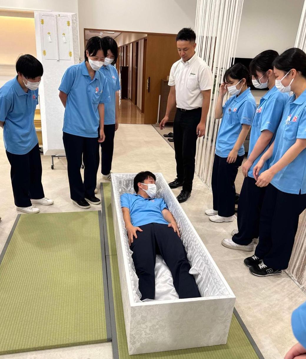 葬儀社で棺桶体験をしている学生達の写真