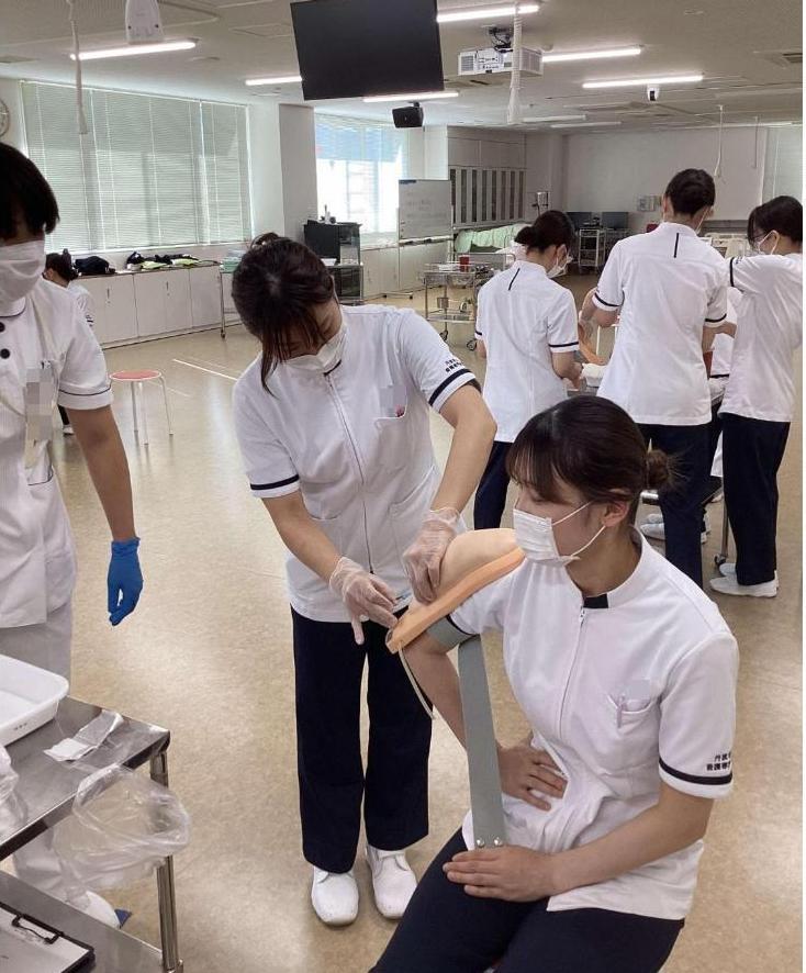 患者役の学生の腕に固定した上腕モデルに注射をしている学生の写真