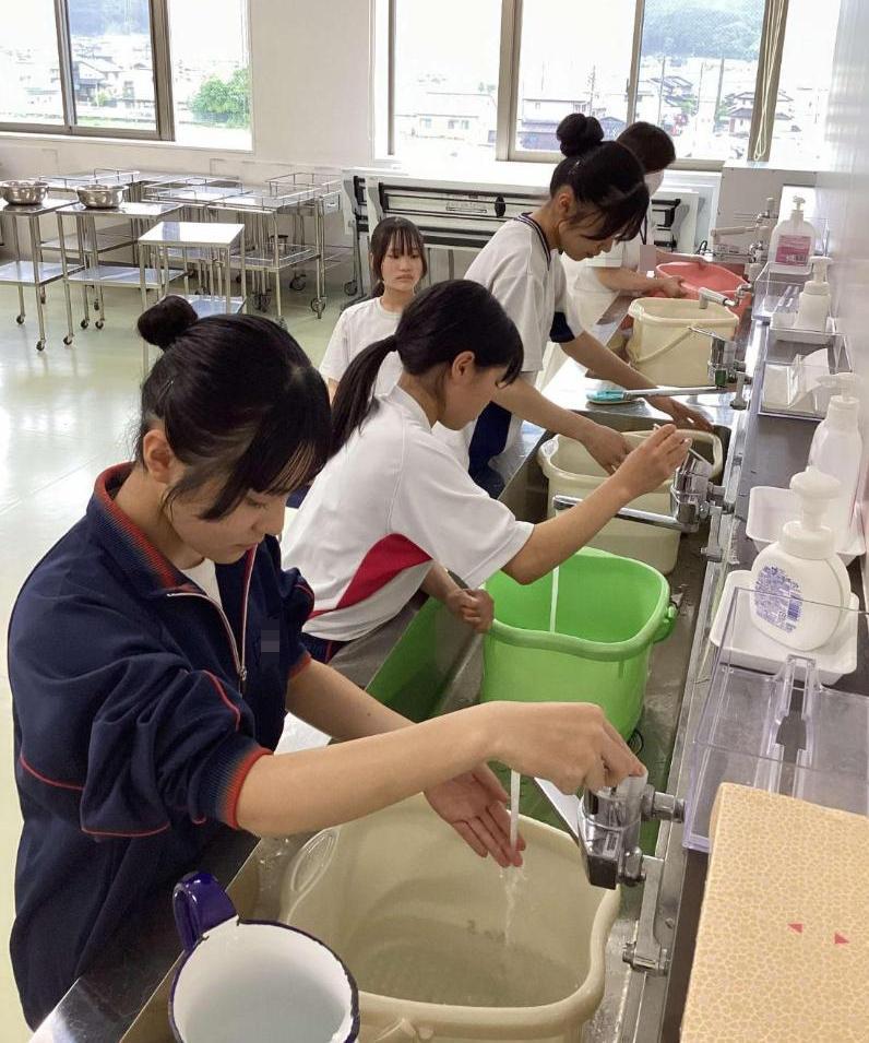 温度をみながら足浴のバケツに湯を入れている中学生達の写真
