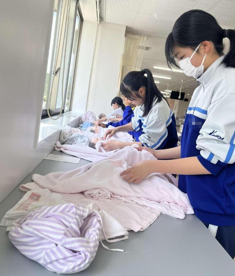 赤ちゃん人形の沐浴が終わって服を着せている中学生達の写真