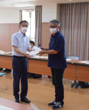 薄い水色のシャツを着た人と紺のシャツを着た人が一緒に書類を持っている写真