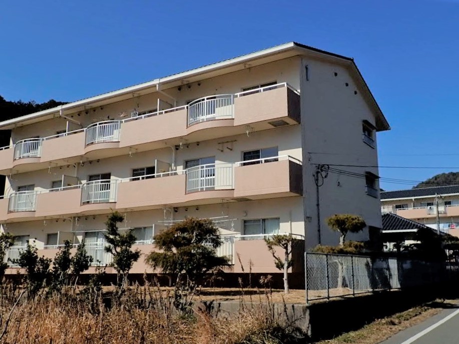 外壁がクリーム色をした3階建ての団地の外観を斜めから撮影した写真