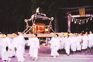 神社の前で白装束の人たちが神輿を担いでいる写真