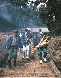 数人で大蛇をかついで、神社の階段を下りている様子の写真