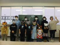 黒板の前で仮面を被った子どもたちなどが並んでいる写真