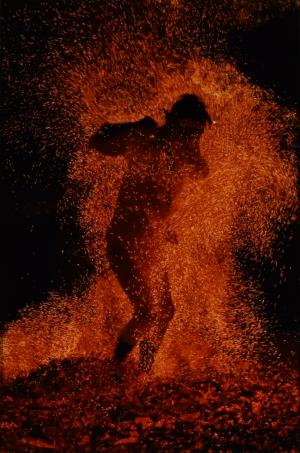 赤く燃えた炭の上の火の粉の中を進む人のシルエットを映した写真