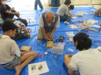 初老の男性の作業を見守る子供たちの写真