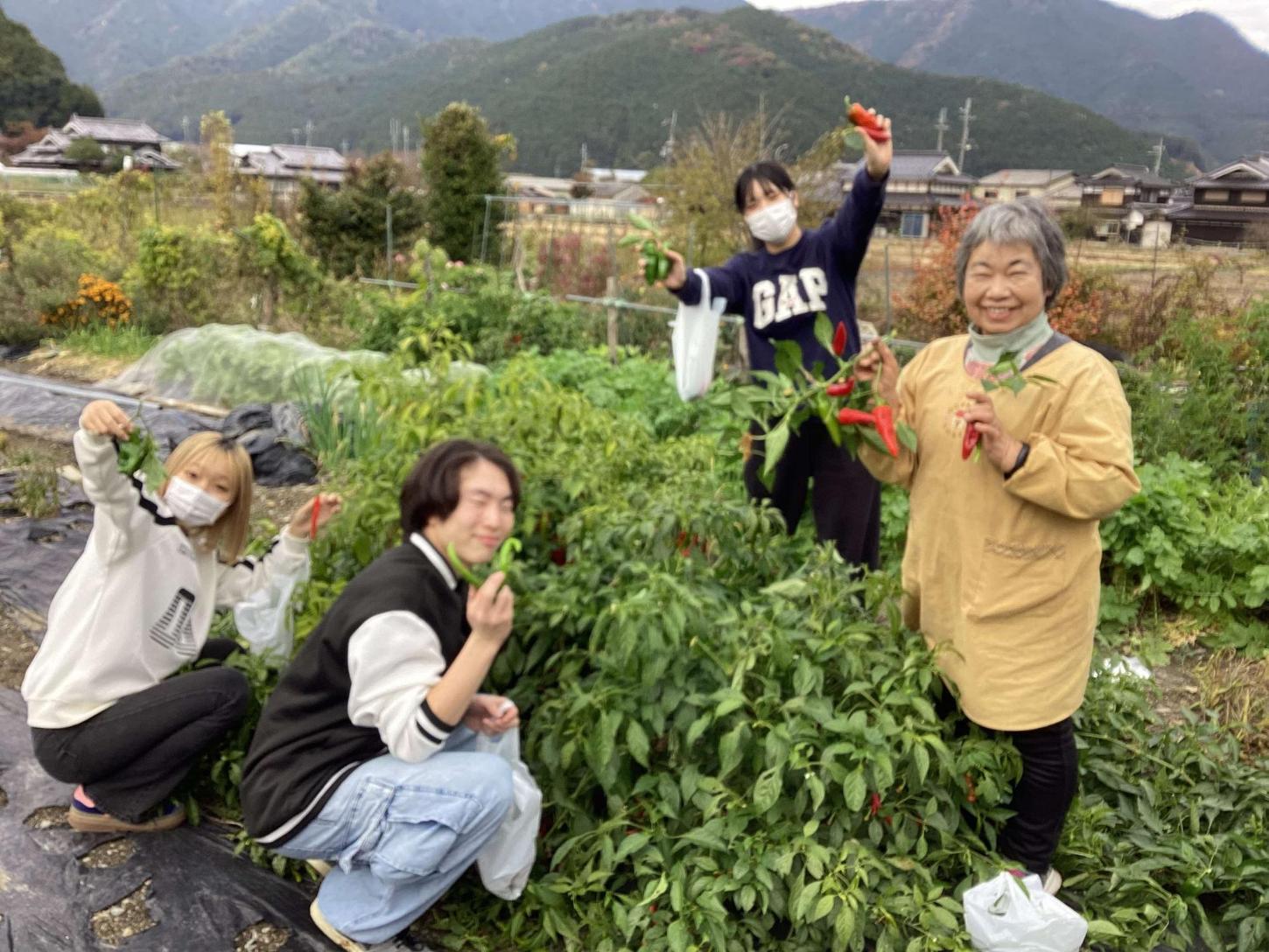 収穫を手伝った後、トウガラシを持って地域の方と学生たちの写真