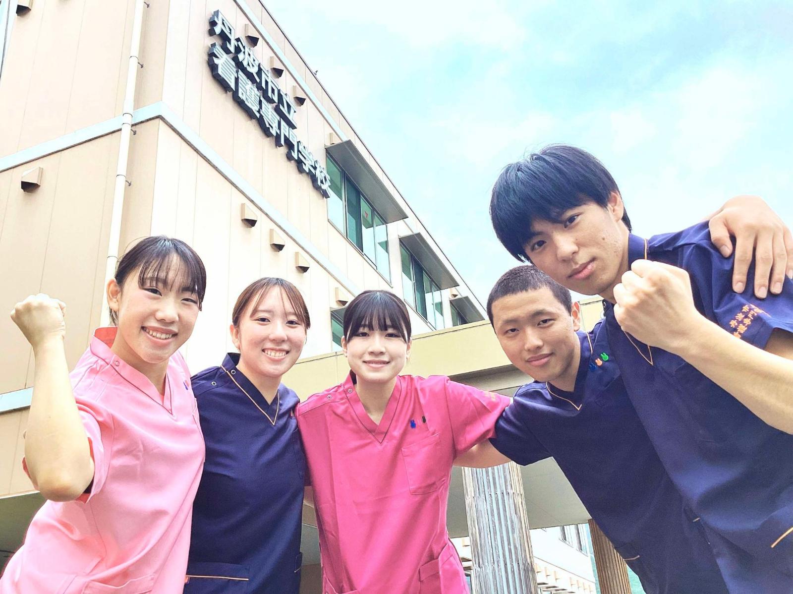 校舎の前で手を広げて笑顔の5人の学生たちの写真
