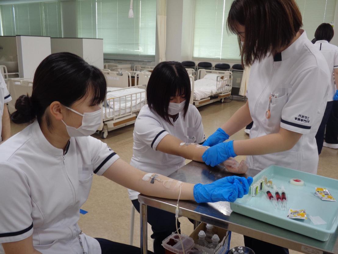 作業台の上に、点滴針を固定した腕を置いている看護学生たちの写真