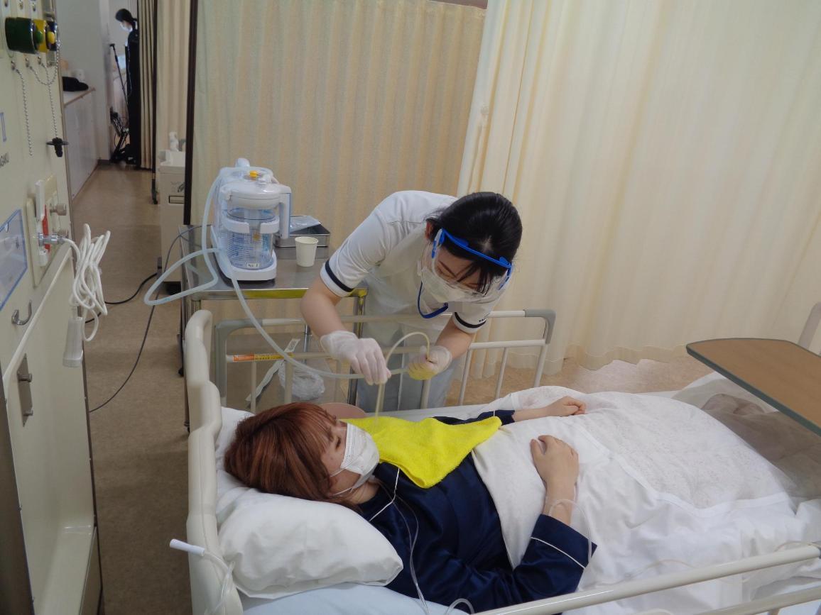 ベッドに横になっている患者役の学生に、吸引器具を近づけている看護学生の写真