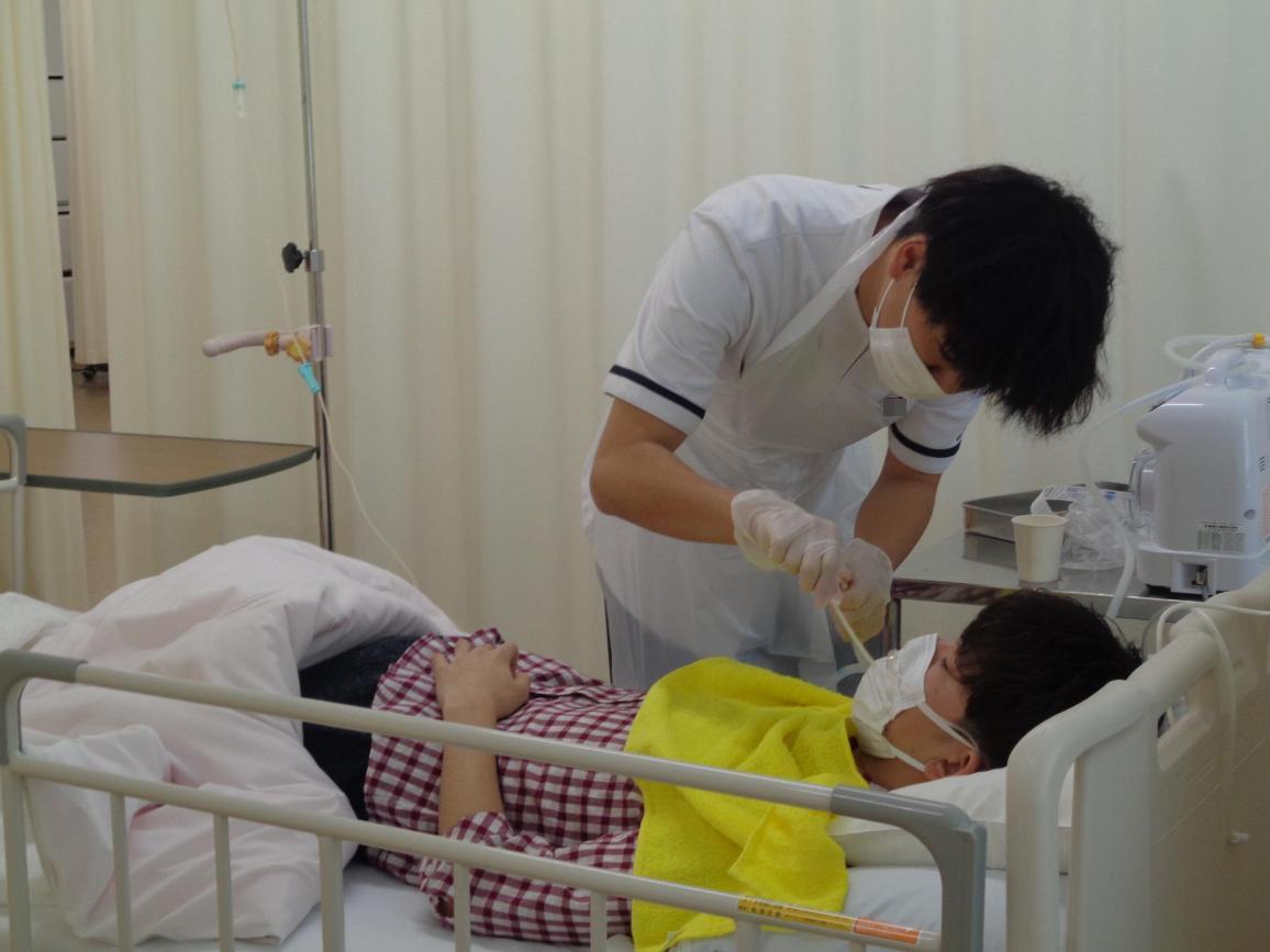 ベッドに寝ている看護学生の脇に立っている看護学生がチューブを持っている写真