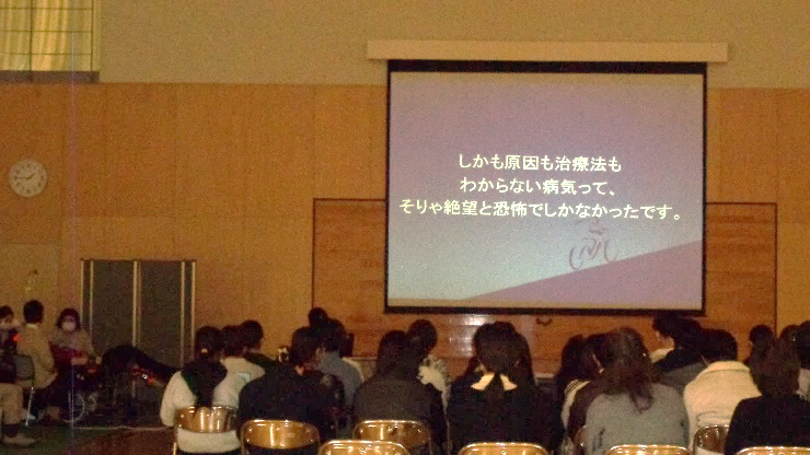 ALS患者さんの気持ち「しかも原因も治療法もわからない病気って、そりゃ絶望と恐怖でしかなかったです。」と映し出されたスクリーンを見ている学生たちの写真