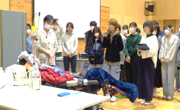 ALS患者さんとの質疑応答をしている学生と、それを聞いている学生たちと患者を見守っているヘルパーの写真