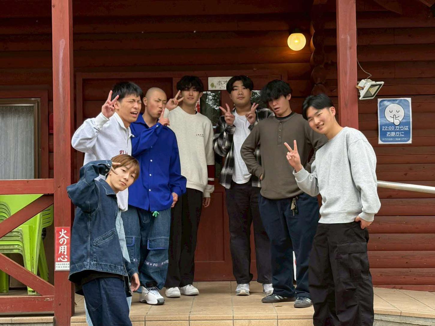 ログハウス前でピースサインをしている男子学生たちの写真