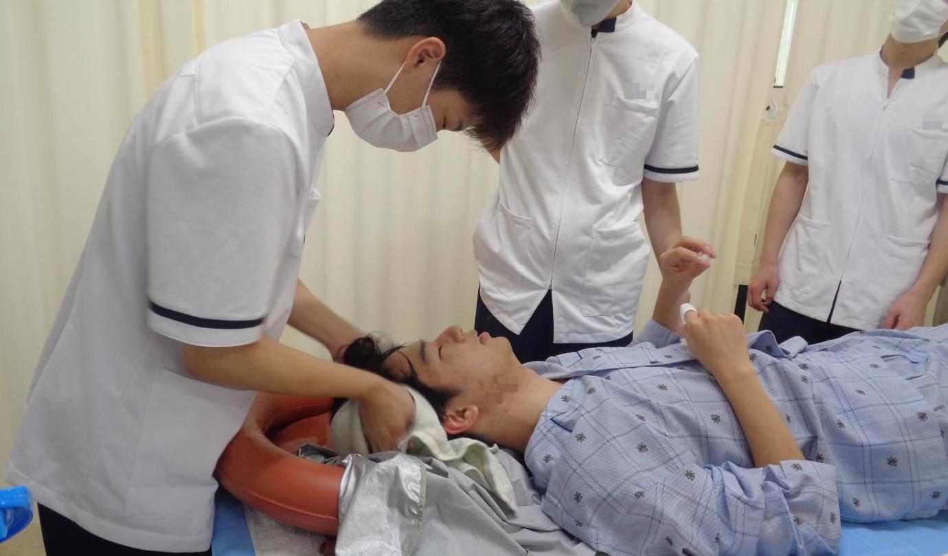 学生がベッド上で学生の洗髪をした後、タオルで髪を拭いているところの写真