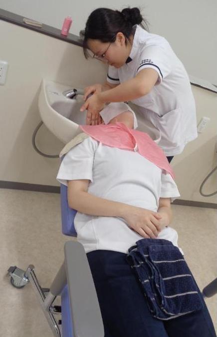 学生が洗髪台の前に仰向けに座った学生の洗髪をしているところの写真