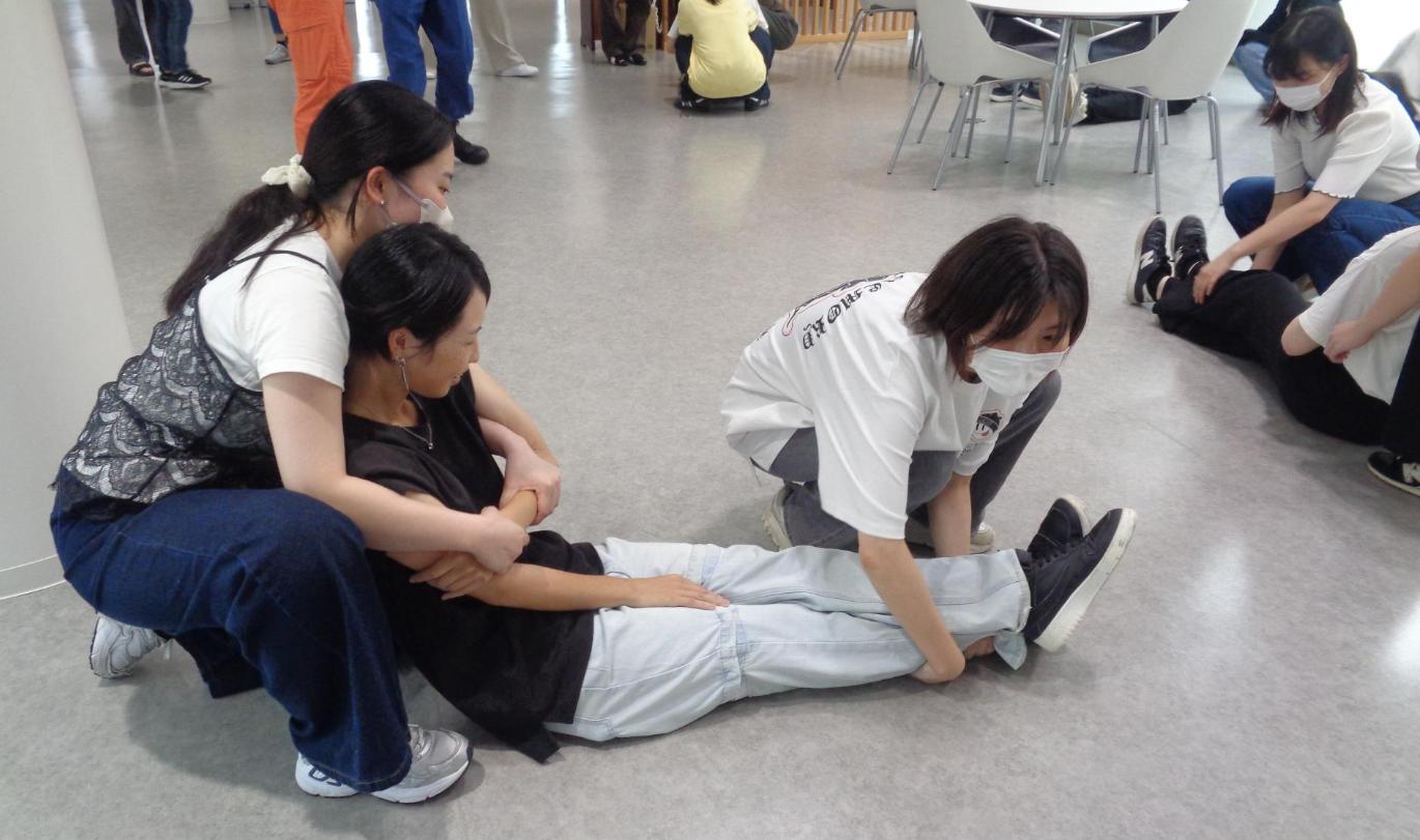 1人が背後から負傷者の腕を固定し、もう1人は足首を持って2人で搬送しようとしている学生たちの写真