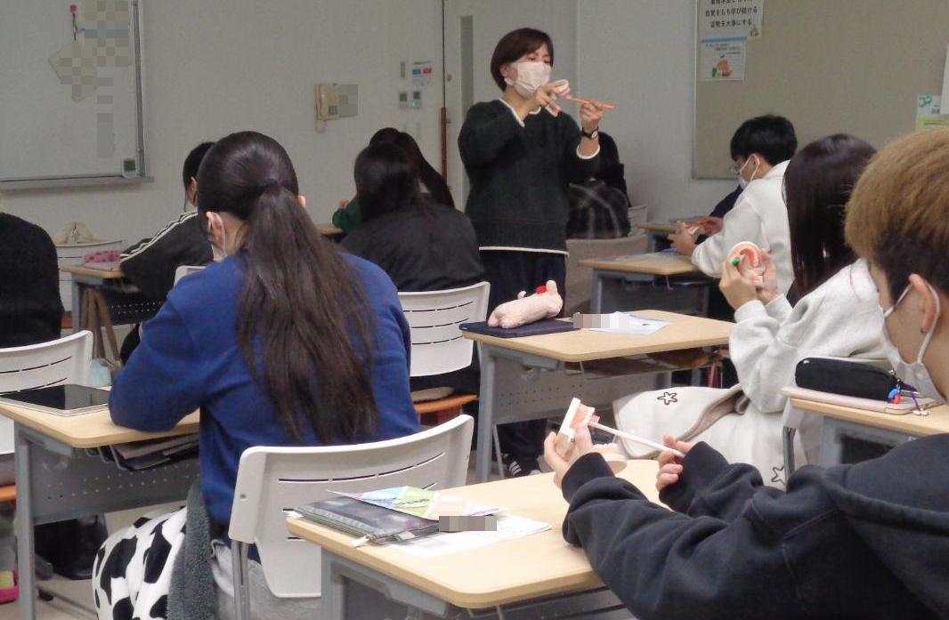 歯科衛生士と学生たちが、歯の模型を歯ブラシで磨いているところの写真
