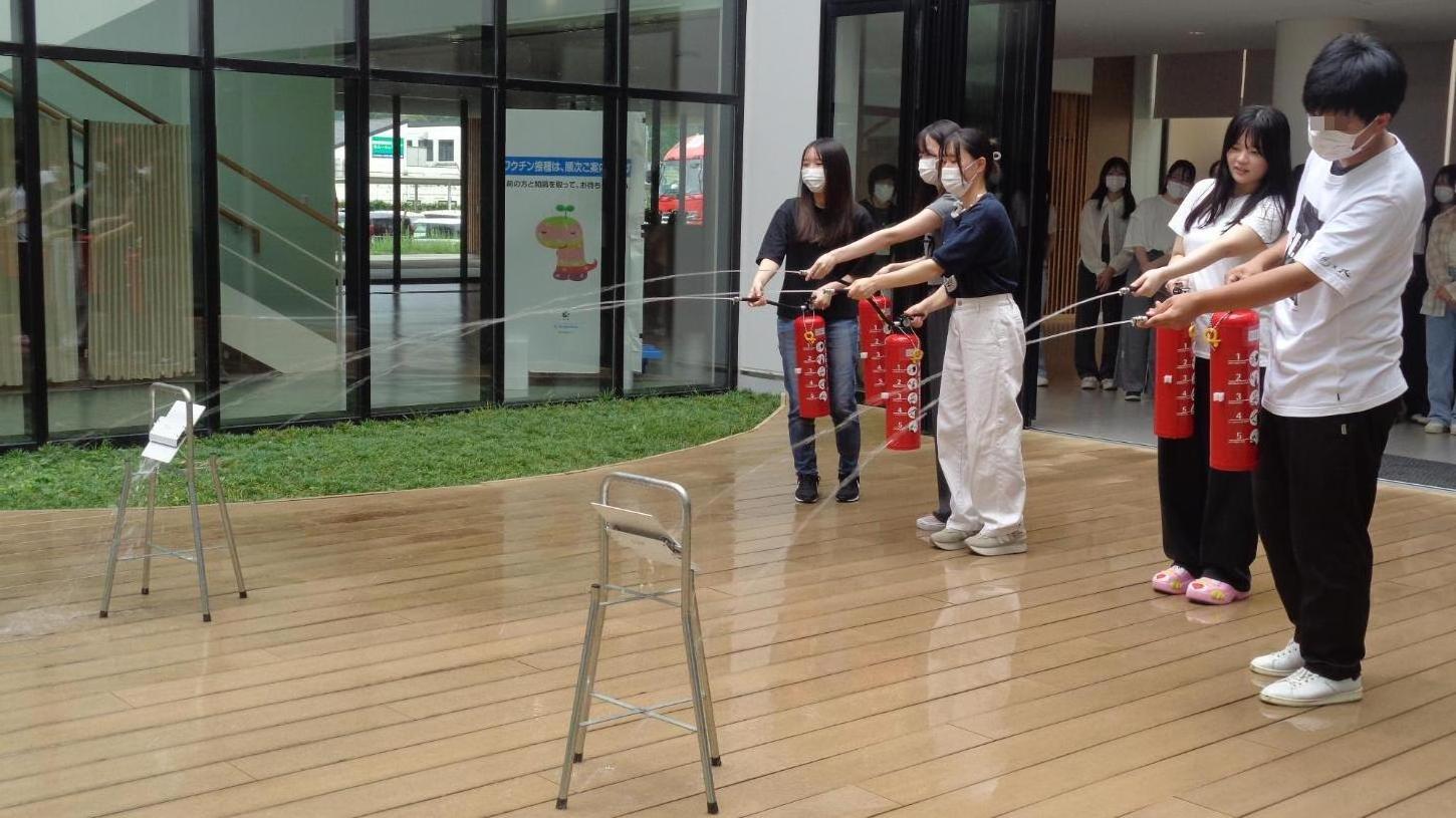 火元の的を目掛けて水消火器の水をかけている学生たちの写真