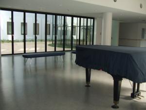 シートで覆われたグランドピアノと椅子が置かれた、広いホール内の写真