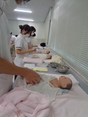 沐浴後の赤ん坊の人形に服を着せている看護学生たちの写真
