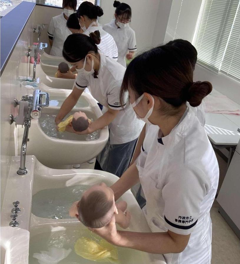 新生児人形の髪と体を洗い終わり、湯船に浸からせたり、浸からせようとしたりしている学生たちの写真