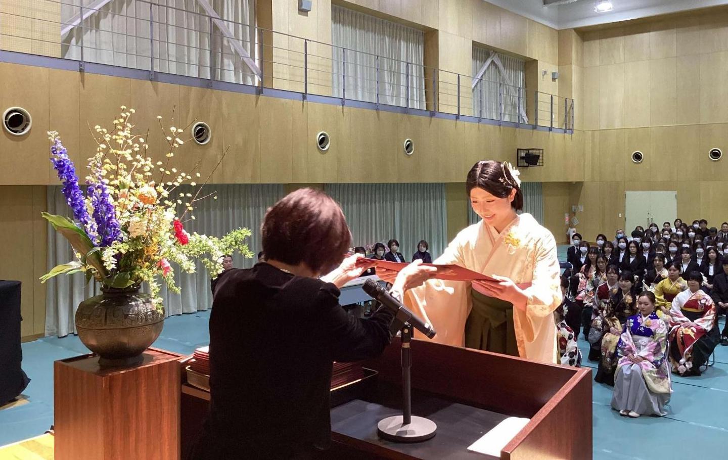 壇上で卒業証書を渡すスーツ姿の校長と、それを受け取る袴姿のにこやかな卒業生の写真