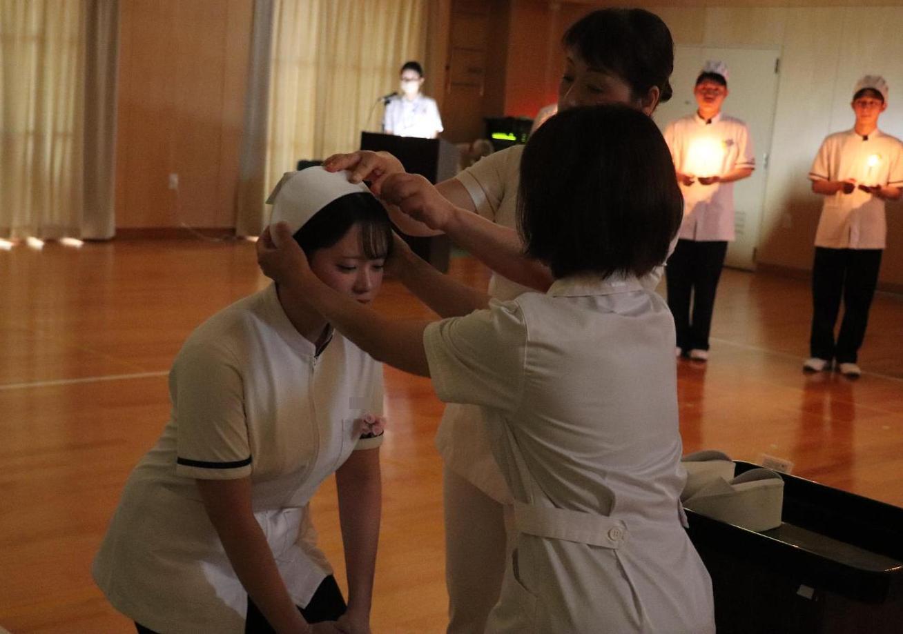 教員2人にナースキャップを頭にかぶせていただいている学生の写真