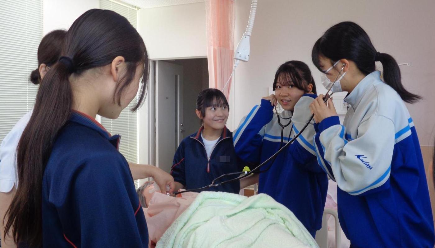 患者役人形の心音を聴診器で聞いている中学生達の写真
