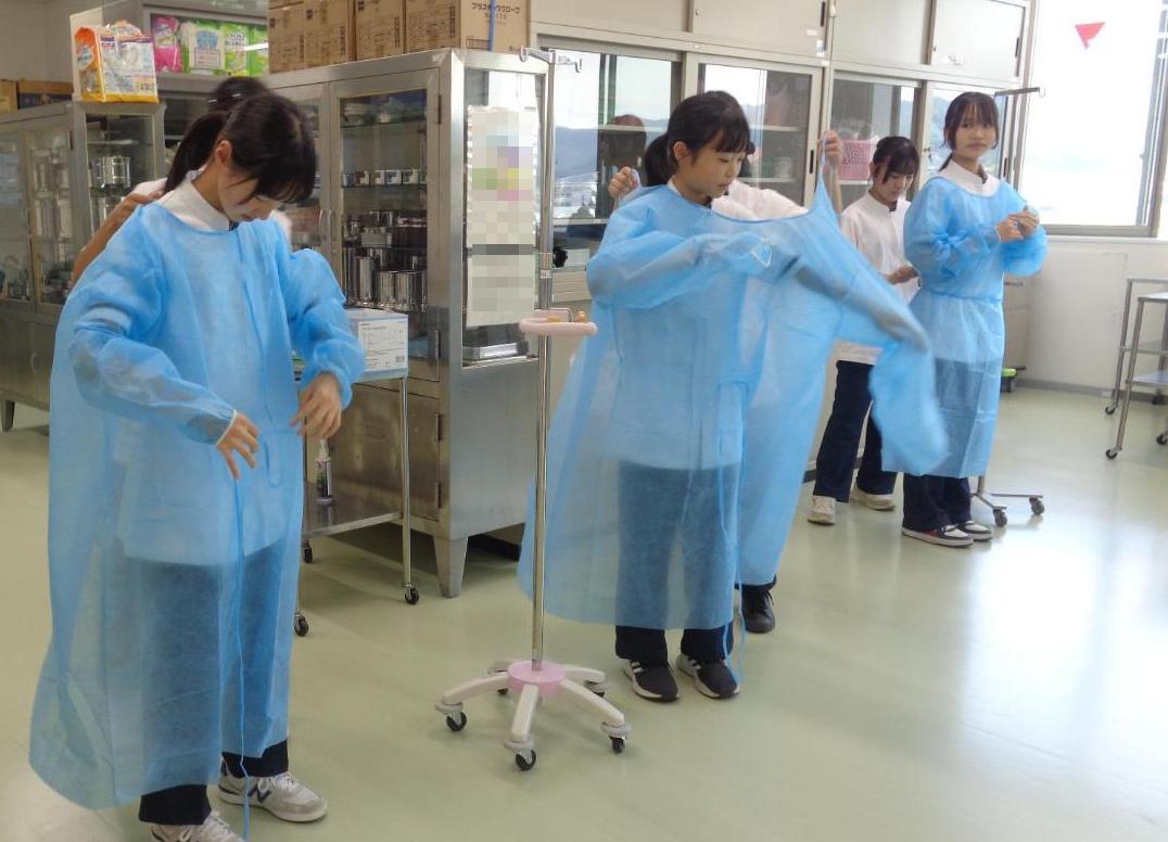 ペアになり紐だけ持ってガウンを着せてもらっている中学生達の写真
