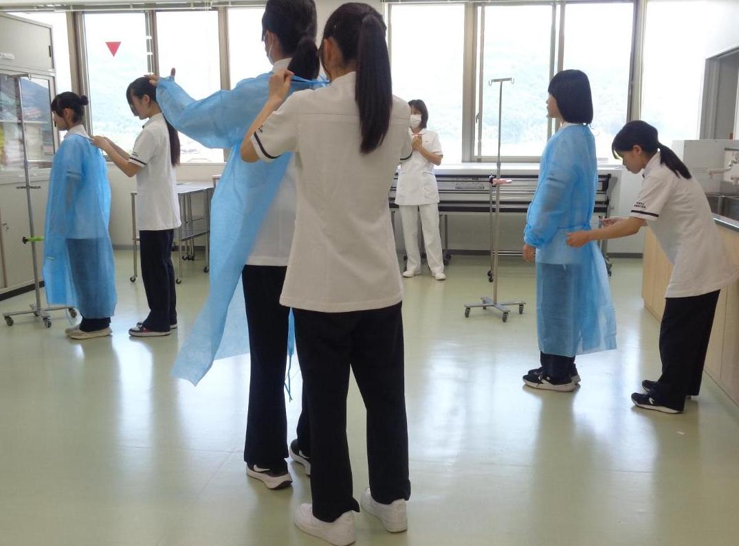 ペアになり紐だけ持ってガウンを着せてもらっている中学生達の写真
