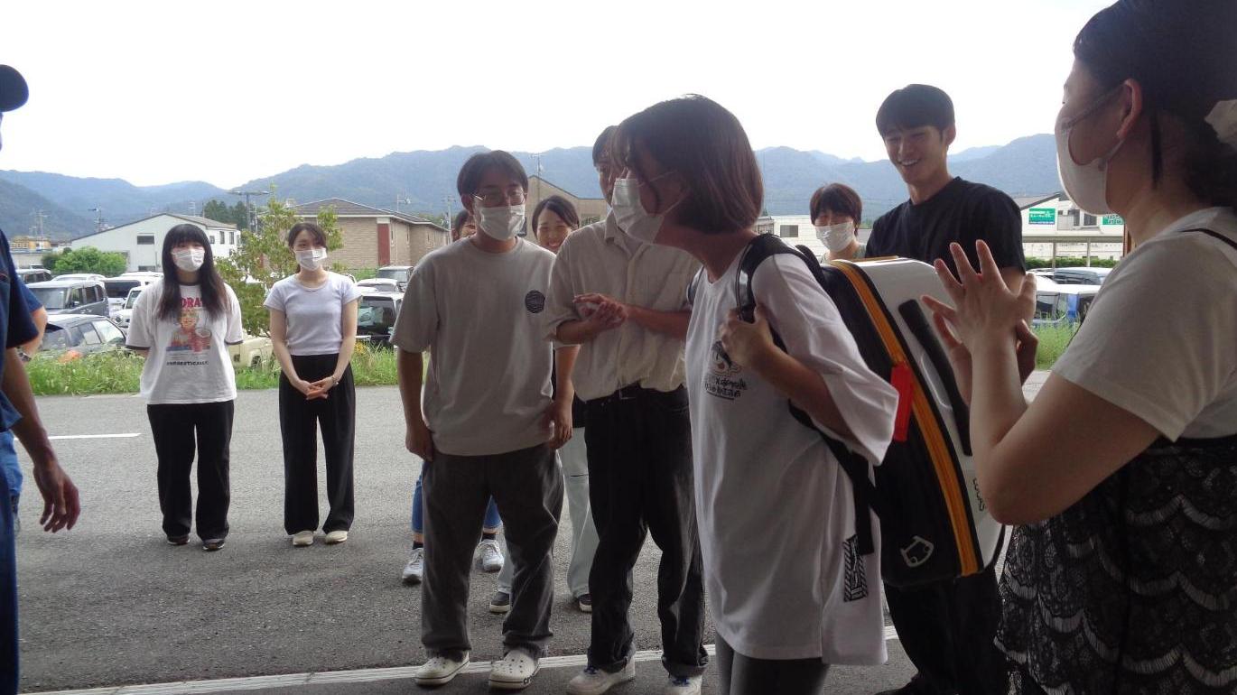 救急車両のLUCAS（ルーカス）を背負っている学生と、それを見ている学生たちの写真