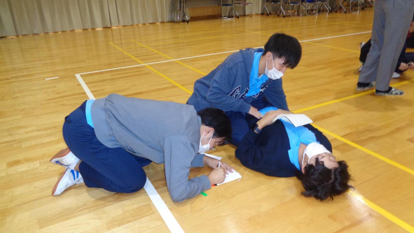 傷病者に具合を聞き、腹部に手を当てている判定者とトリアージ紙に記入している記録者の3人の写真