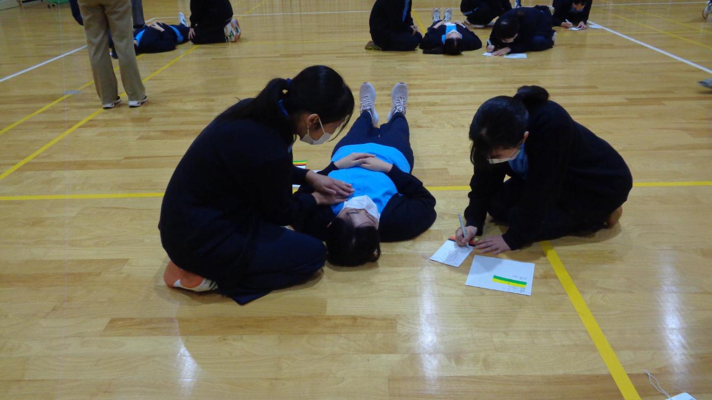 傷病者に具合を聞き、胸部に両手を当てている判定者とトリアージ紙に記入している記録者の3人の写真