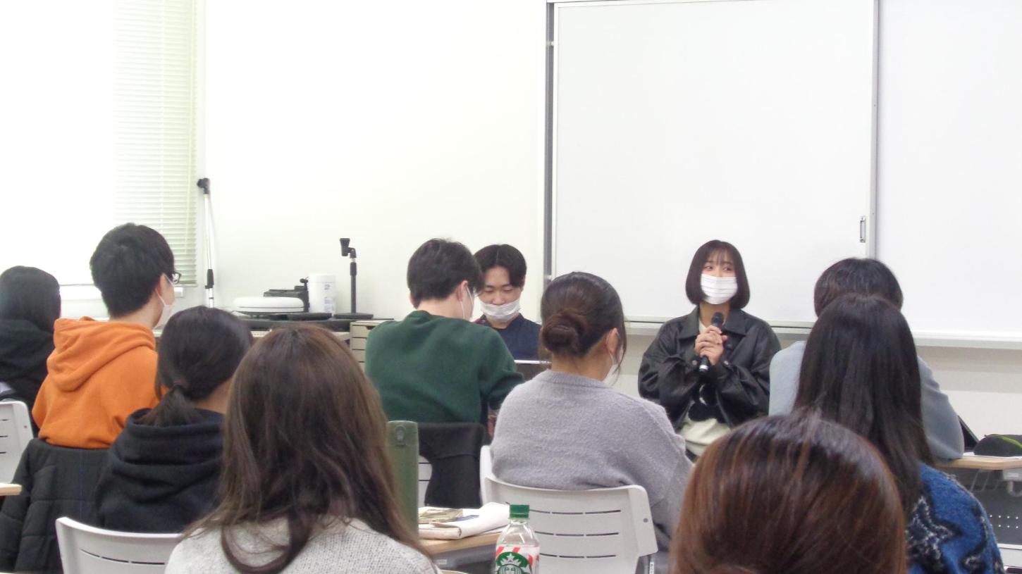 卒業生がマイクを持って、後輩の学生たちに、試験勉強についてアドバイスを話している写真