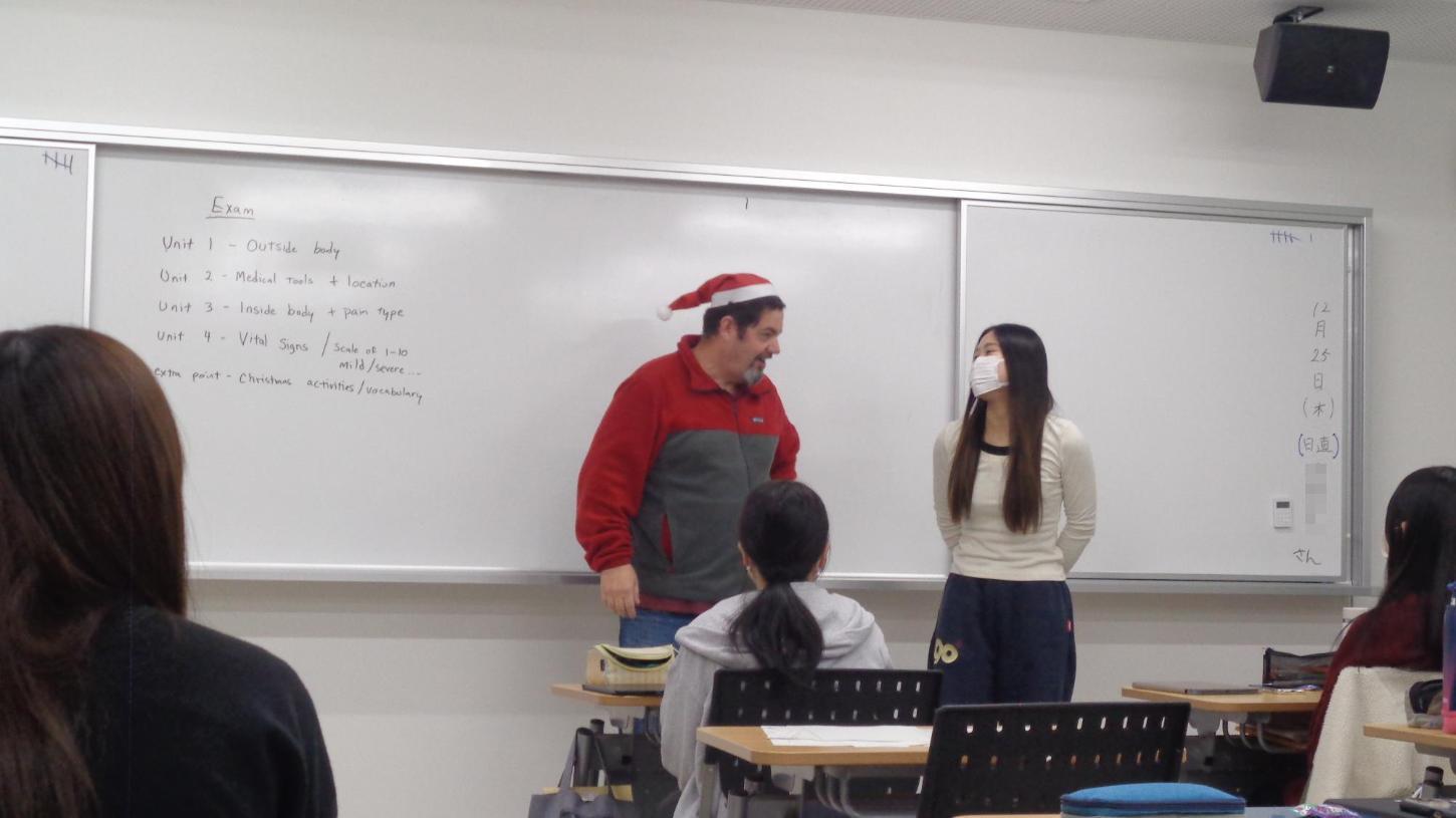 サンタクロースの帽子を被った英会話講師と学生がジェスチャーをしようとしている写真
