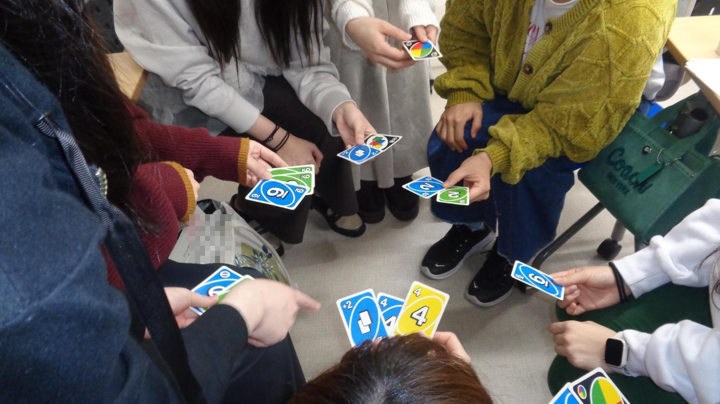 カードゲームの手札を見せて、どのカードを出そうかと、相談している学生たちの写真