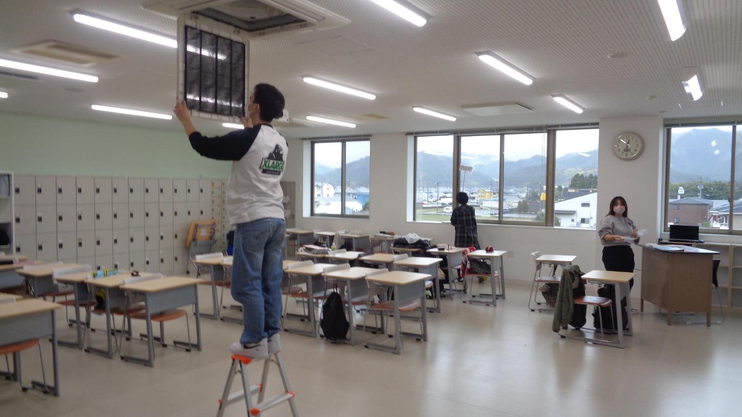 教室のエアコンフィルターを取り外している学生と、窓ガラスを掃除している学生たちの写真