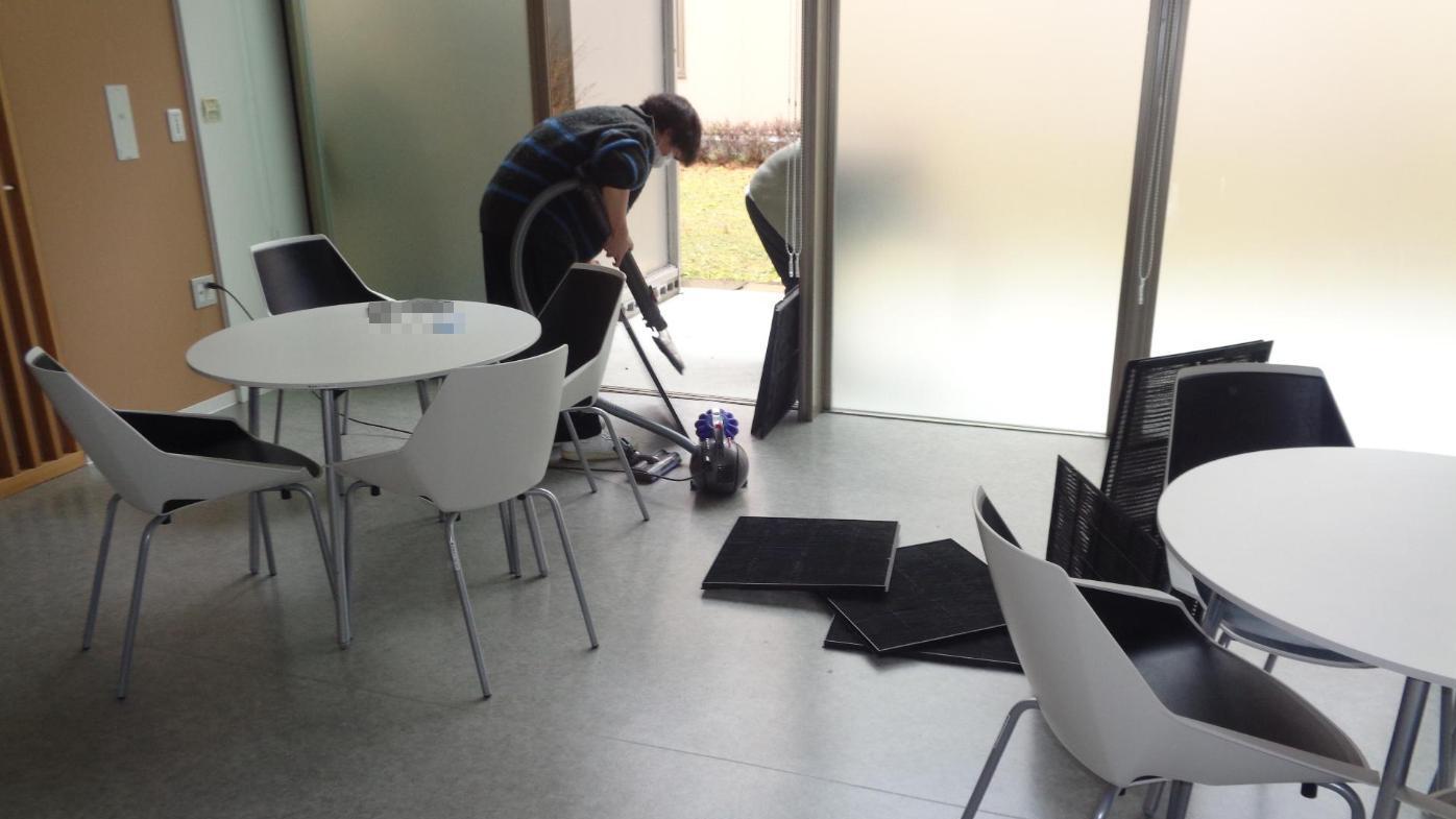 取り外したエアコンフィルターのほこりを、掃除機で吸い取ろうと、屋外へ出ようとしている学生たちの写真