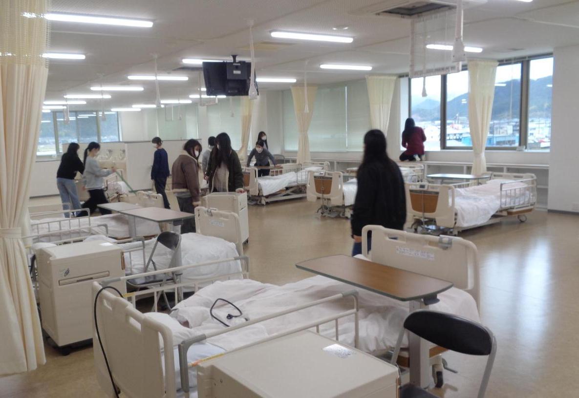 実習室のベッドを移動して床掃除したり、窓ガラスのレールを掃除したりしている学生たちの写真