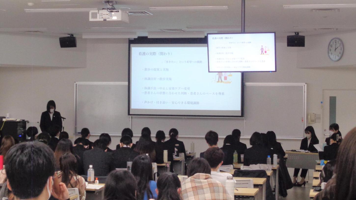 スクリーンの隣で発表している学生と、聴講している学生たちの写真