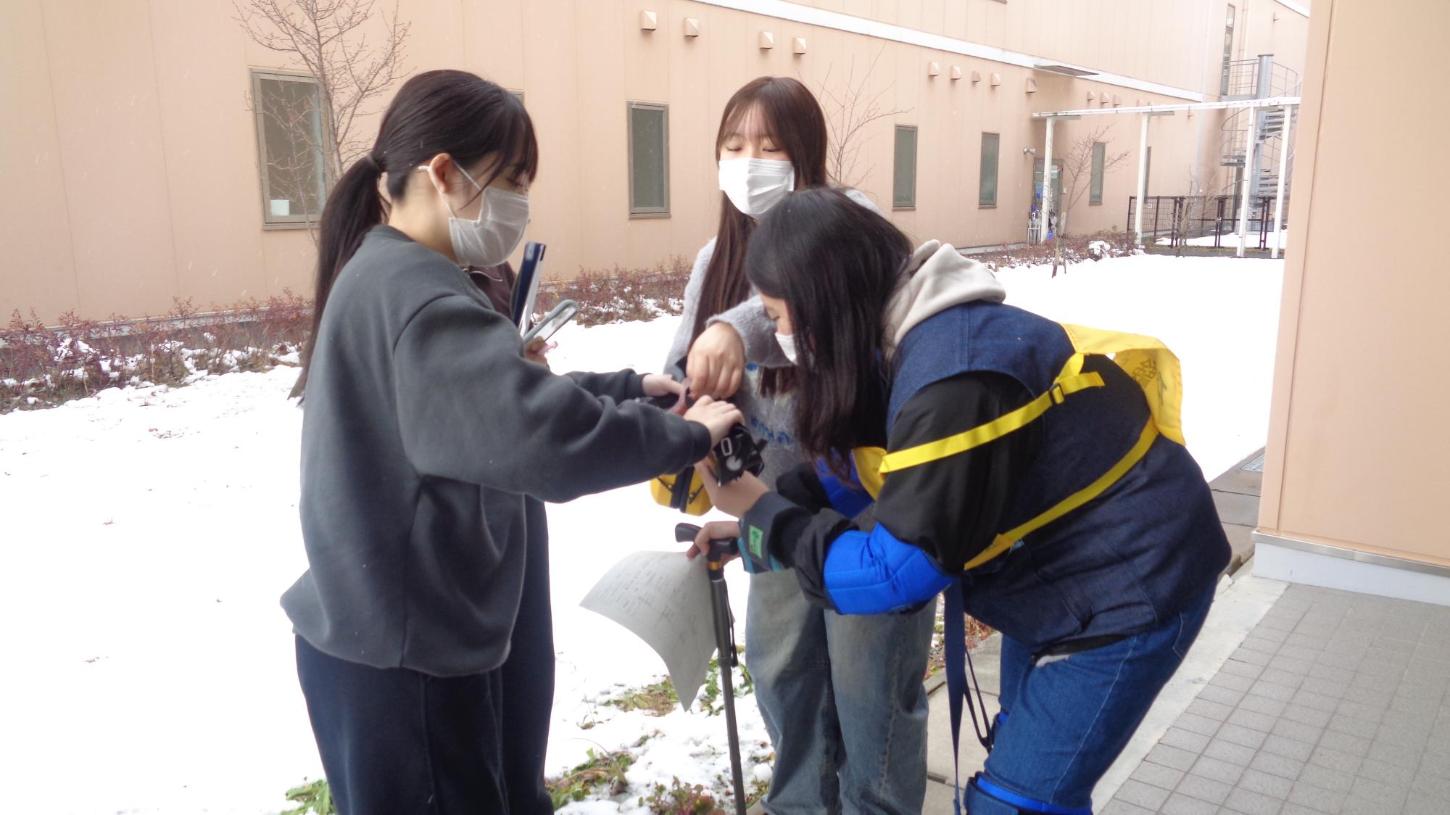 老化体験スーツを着た学生が、ゴーグルを付け替えようとグループの学生に手伝ってもらっているところの写真