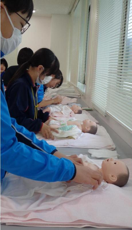 赤ちゃん人形の沐浴が終わって服を着せている中学生達の写真