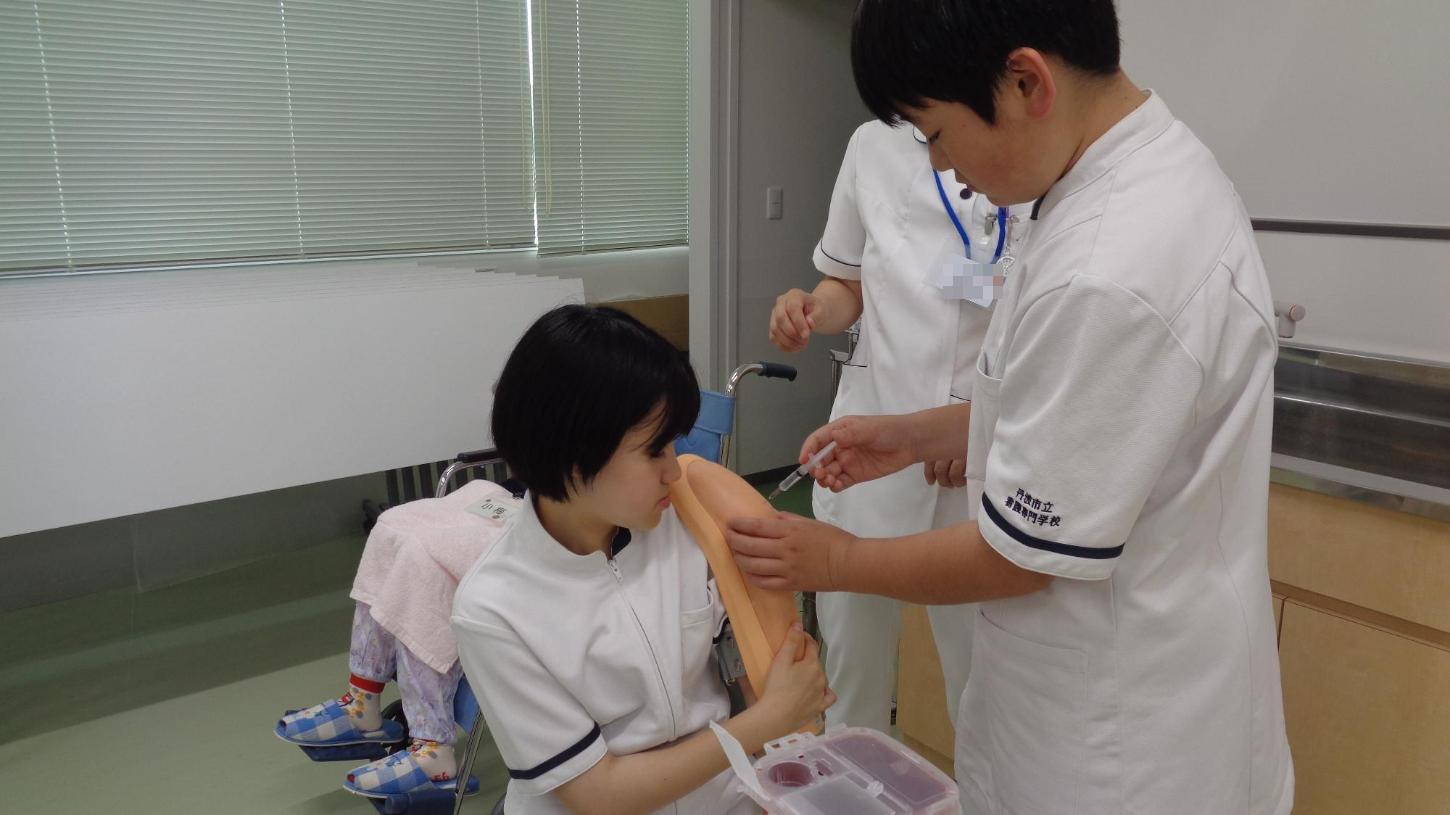 腕にパッドを当てた中学生へ、液の入っていない注射器で筋肉注射をしている中学生の写真