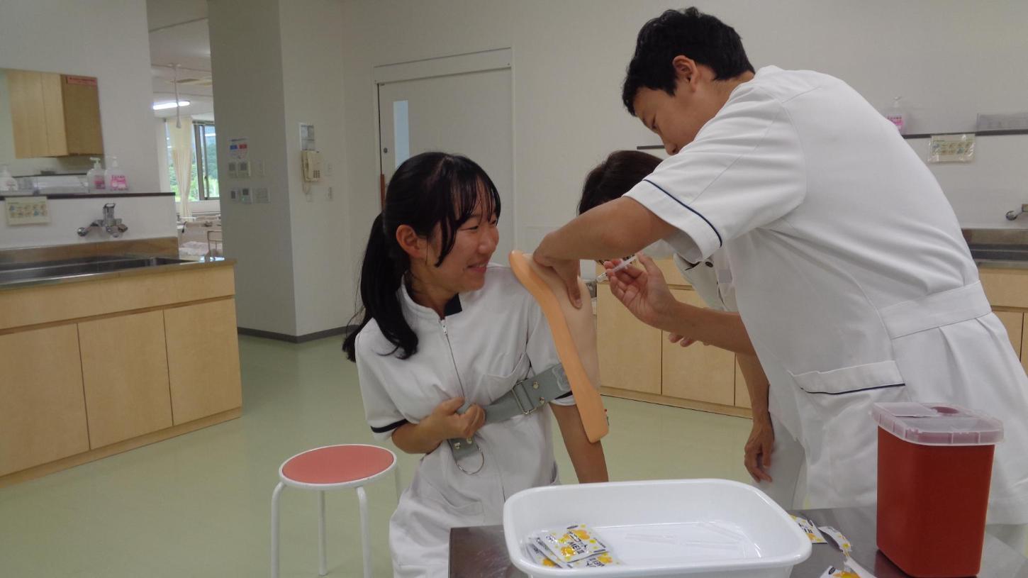 パッドを当てた中学生の腕に、液の入っていない注射器で筋肉注射をしている中学生の写真