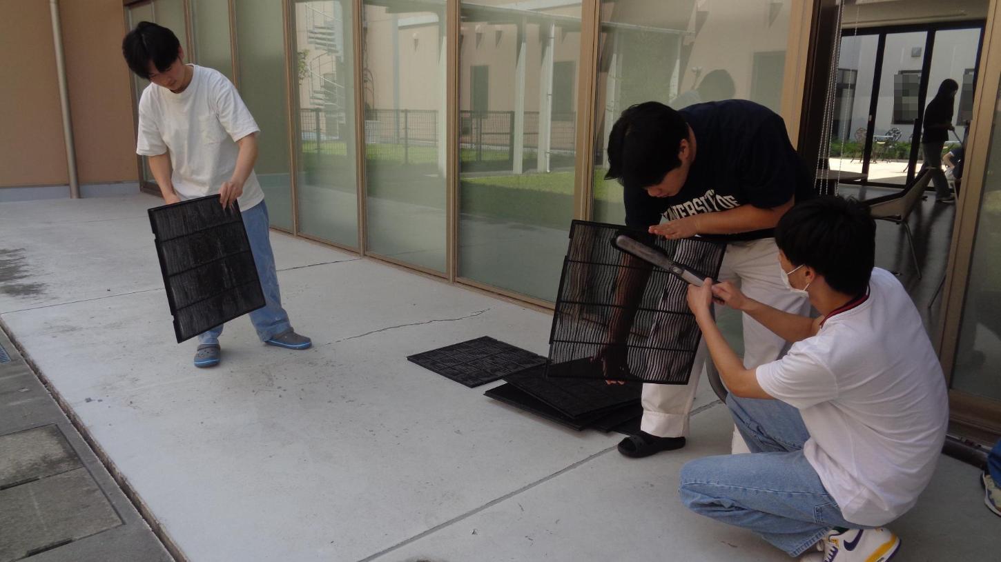 エアコンフィルターを掃除機で掃除している学生たちの写真