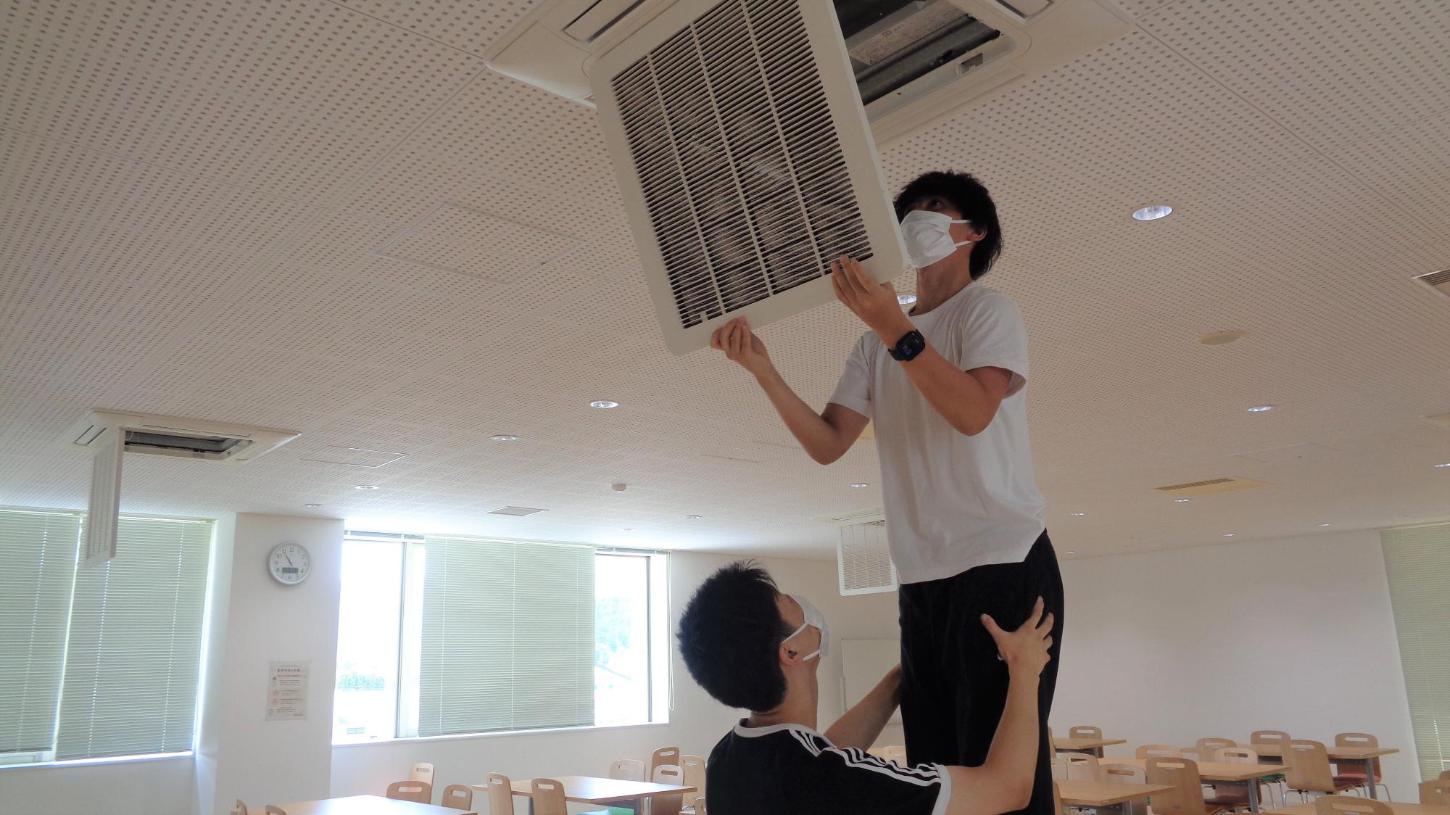 食堂のエアコンフィルターの取り外している学生たちの写真