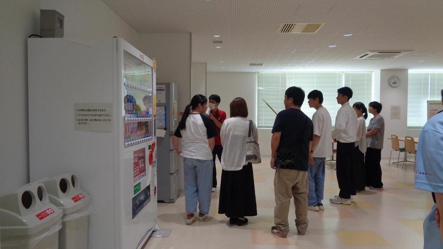 学生がキャンパスツアーで食堂の中を案内し、冷蔵庫の使い方について参加者たちに説明しているところの写真